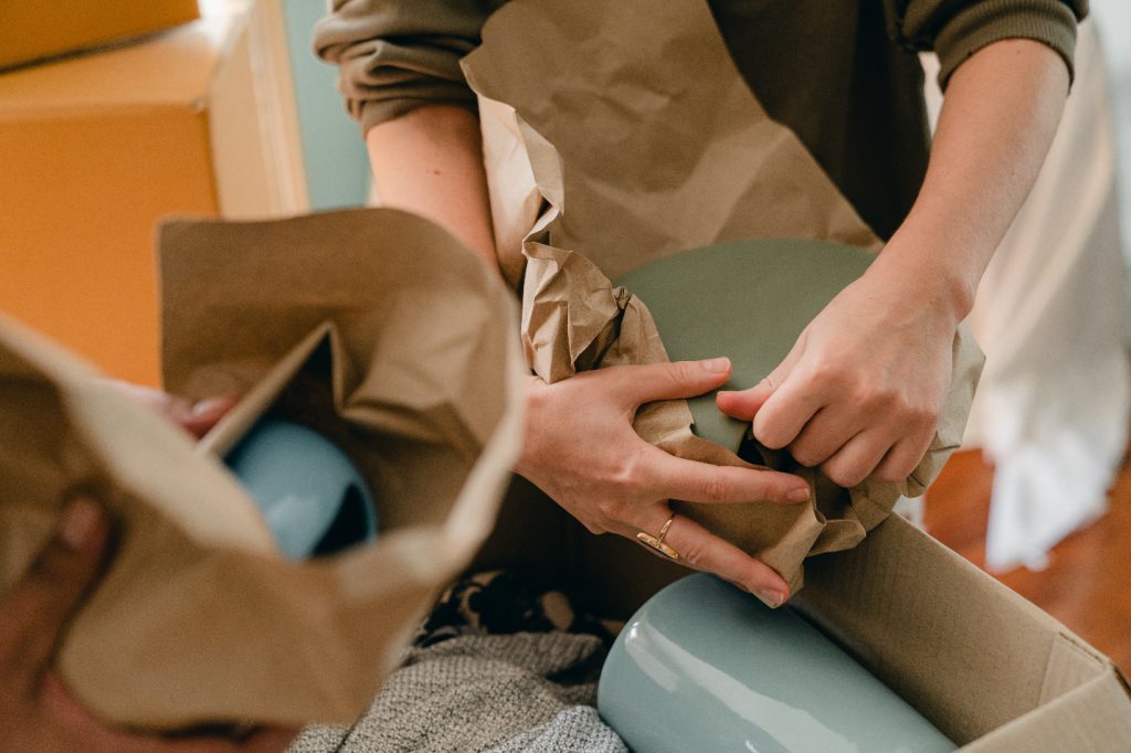 Unrecognizable Person Packing Ceramic Tableware in Parchment