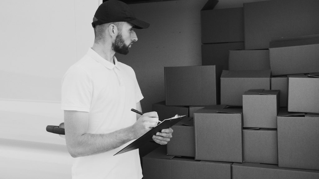 Grayscale Photo of a Man Looking At Packaging Boxes